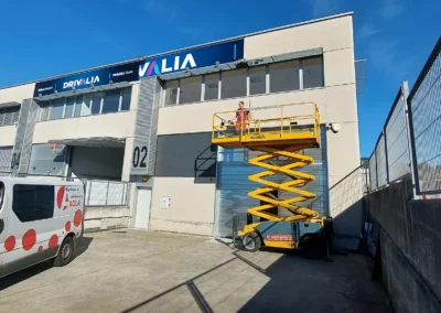 Instalación de rótulo corporativo de fachada de Drivalia / Valia en una nave o fachada industrial con plataforma elevadora.