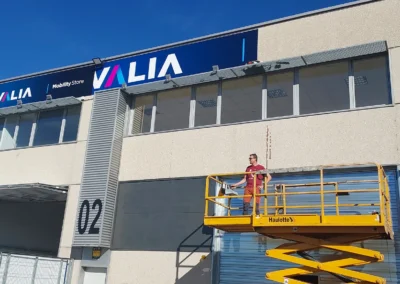 Instalación de rótulo corporativo de fachada de Drivalia / Valia en una nave o fachada industrial con plataforma elevadora.