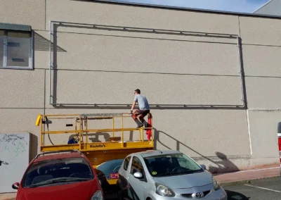 Instalación de estructura tubular para lona en una nave o fachada industrial con plataforma elevadora.