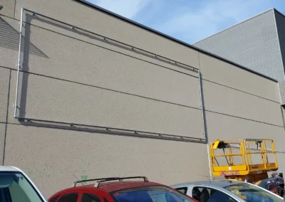 Instalación de estructura tubular para lona en una nave o fachada industrial con plataforma elevadora.
