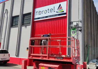 Instalación de rótulo de nave de Fibrotel en una nave o fachada industrial con plataforma de tijera.