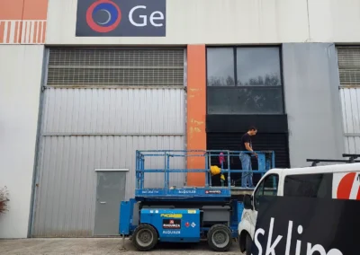 Instalación de rótulo corporativo de fachada de Gesklima en una nave o fachada industrial con plataforma elevadora.