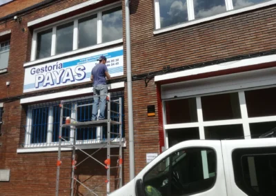 Instalación de rótulo de fachada de Gestoría Payas en una nave o fachada industrial con andamio móvil.
