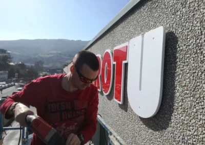 Instalación de letras corpóreas en una nave o fachada industrial con plataforma elevadora.