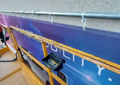 Instalación de lona de gran formato con marco tubular en una nave o fachada industrial con plataforma elevadora.