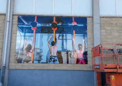 Instalación de paneles gráficos de gran formato de centro deportivo en una nave o fachada industrial con plataforma elevadora.