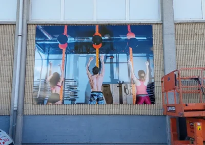 Instalación de paneles gráficos de gran formato de centro deportivo en una nave o fachada industrial con plataforma elevadora.
