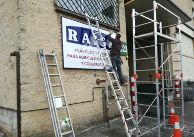 Instalación de rótulo de fachada industrial de RAISA en una nave o fachada industrial con andamio y escaleras.