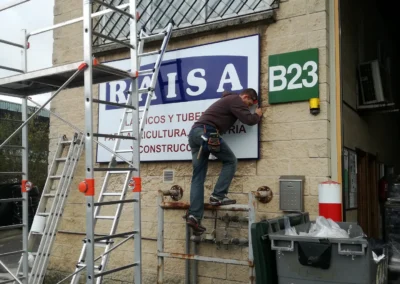 Instalación de rótulo de fachada industrial de RAISA en una nave o fachada industrial con andamio y escaleras.
