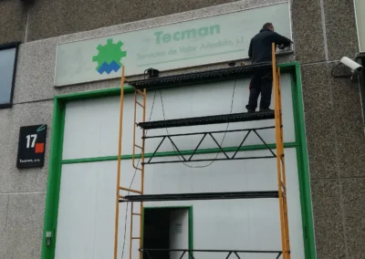 Instalación de rótulo de nave de Tecman en una nave o fachada industrial con andamio.